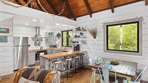 A modern kitchen with a central island, bar stools, and a dining table with a view of the outdoors.