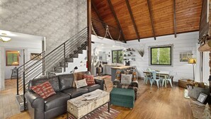 A spacious living area with a high ceiling, a staircase, a kitchen, and a dining area.