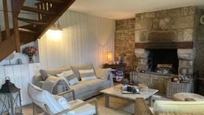 Ein gemütliches Wohnzimmer mit einer Couch, Sesseln, einem Couchtisch und einem Kamin aus Stein.