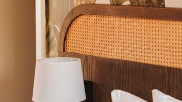 A neatly made hotel room with a bed, a bedside table with a lamp, a clock, and a pillow.