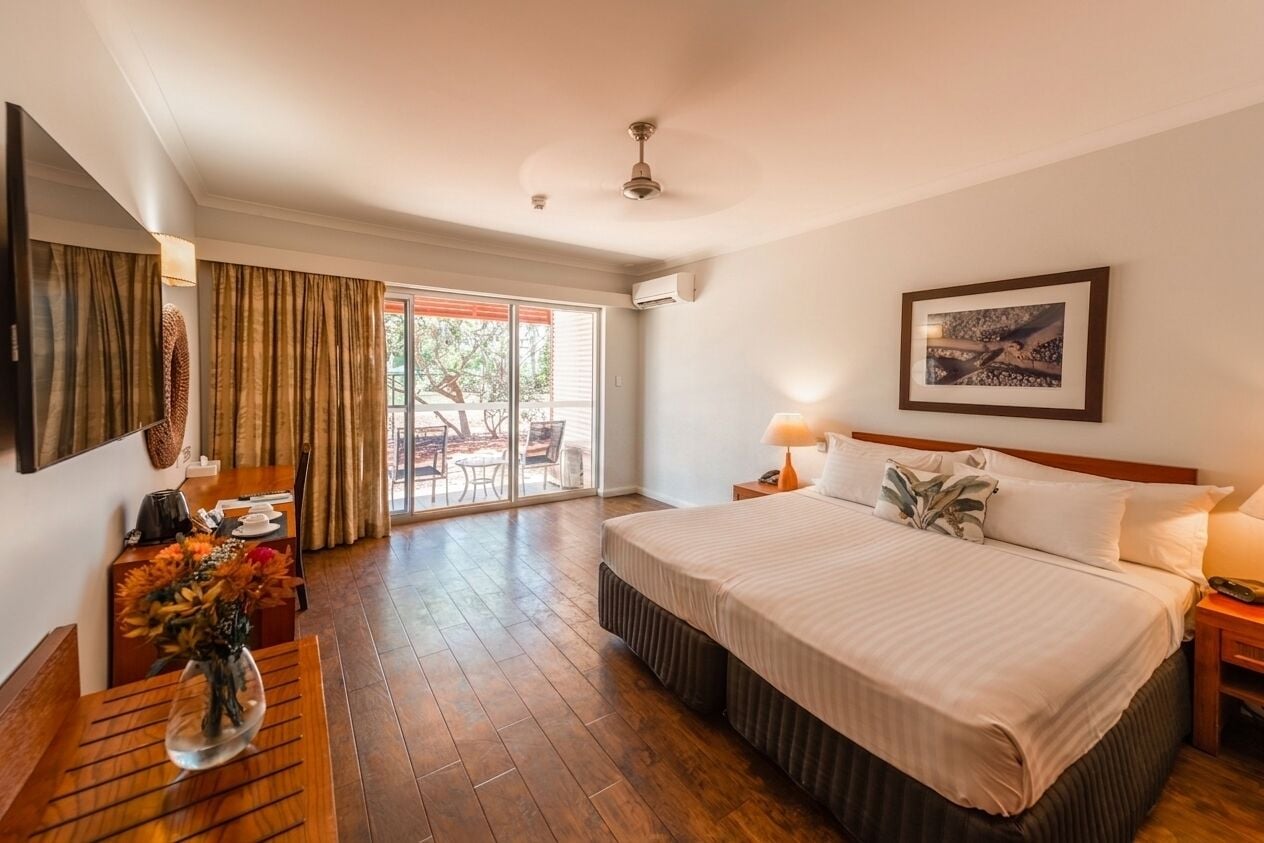 Ein Hotelzimmer mit Bett, Nachttisch, Lampe, Kunstwerk und Blick ins Freie.