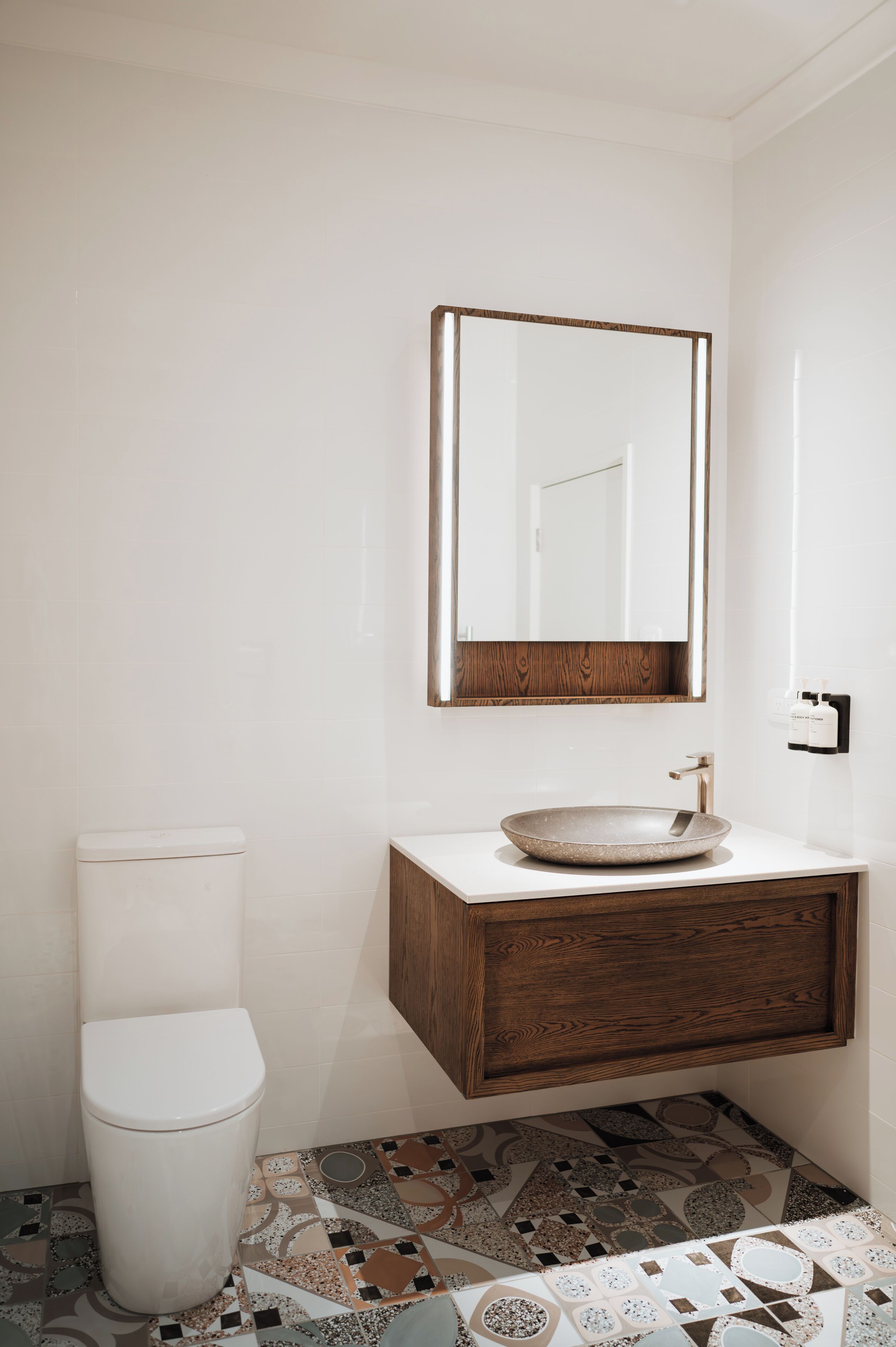 A bathroom with a white toilet, a wooden vanity with a round sink, and a mirror above it.