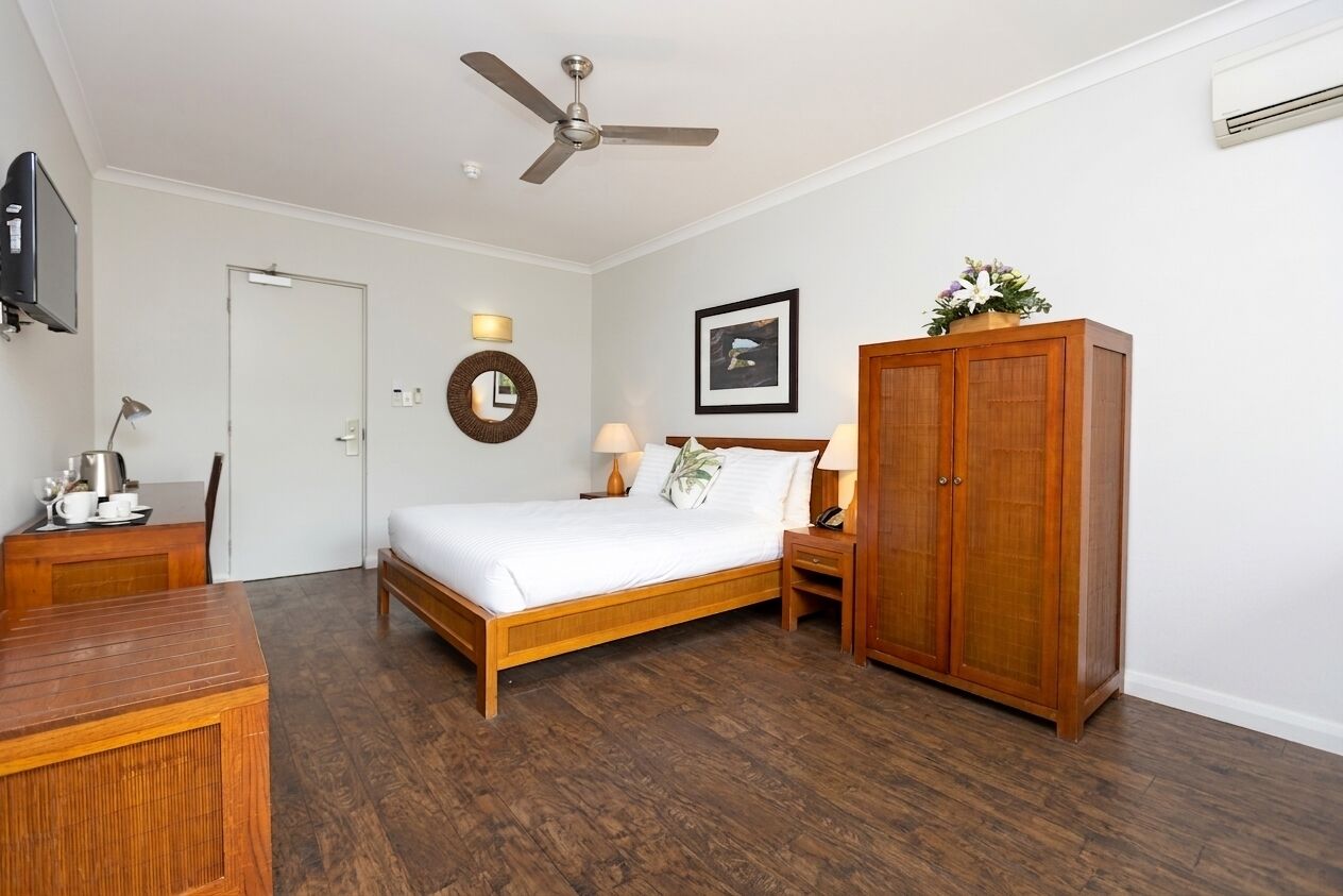 A hotel room with a bed, bedside table, lamp, wardrobe, and a ceiling fan.