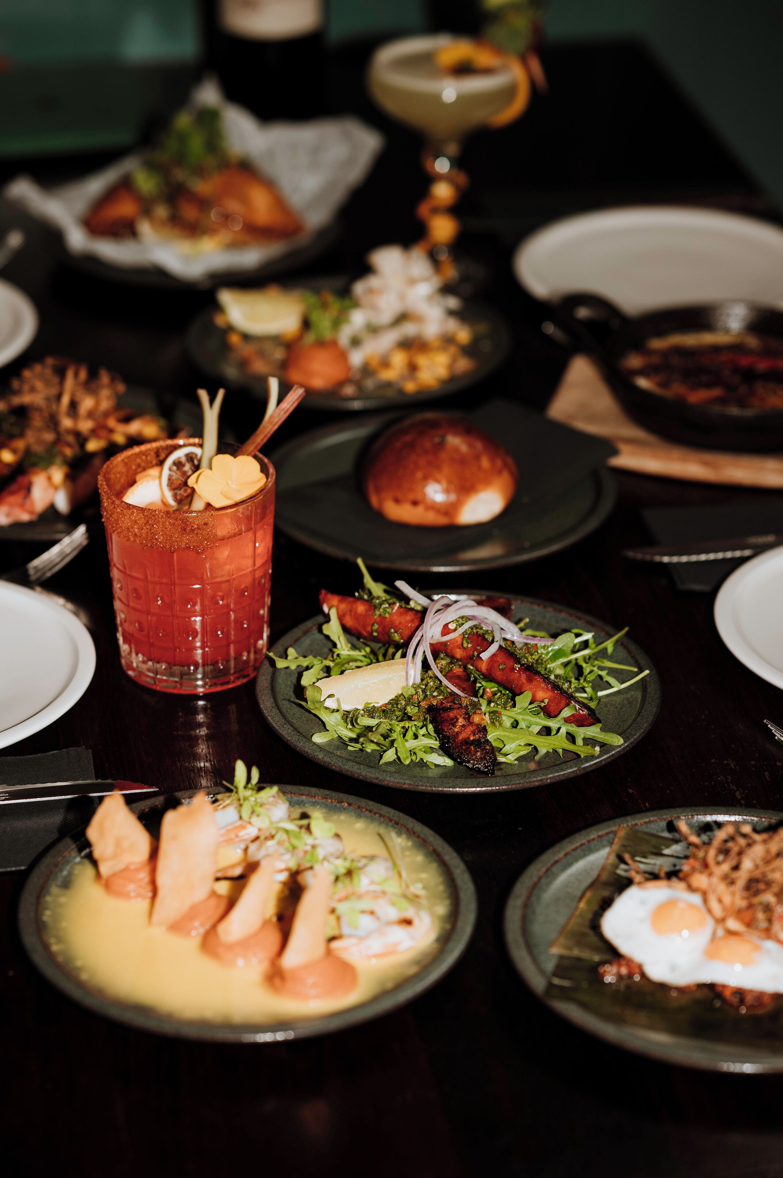 A dining table with various dishes, including a glass of iced tea with a heart-shaped garnish, a plate with grilled meat and vegetables, and other assorted foods.