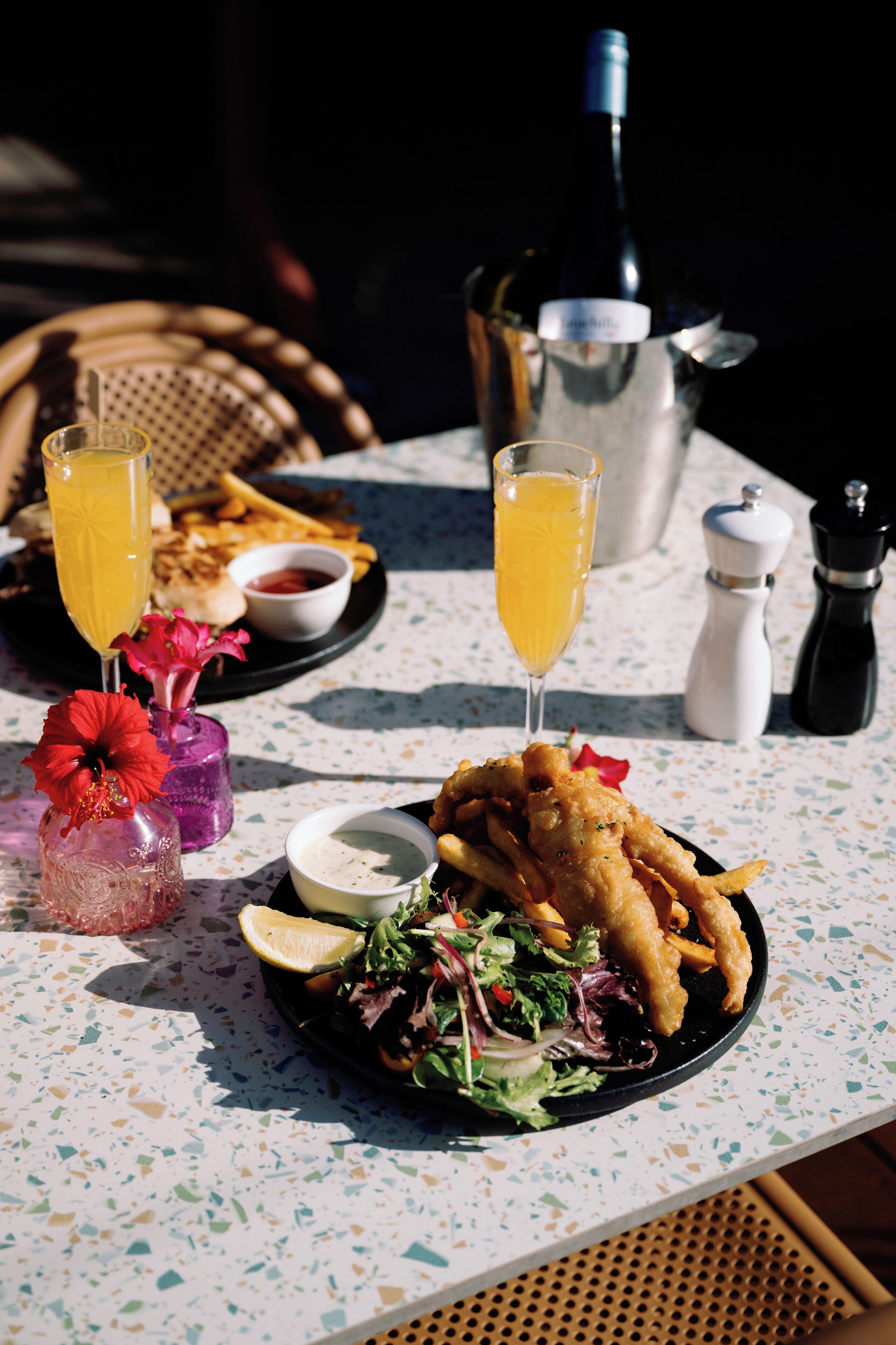 A table with a plate of food, a bottle of wine, and two glasses of orange juice.