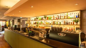 A bar area with a long counter, shelves of various liquor bottles, and a coffee machine. - The Continental Hotel Broome (Broome)