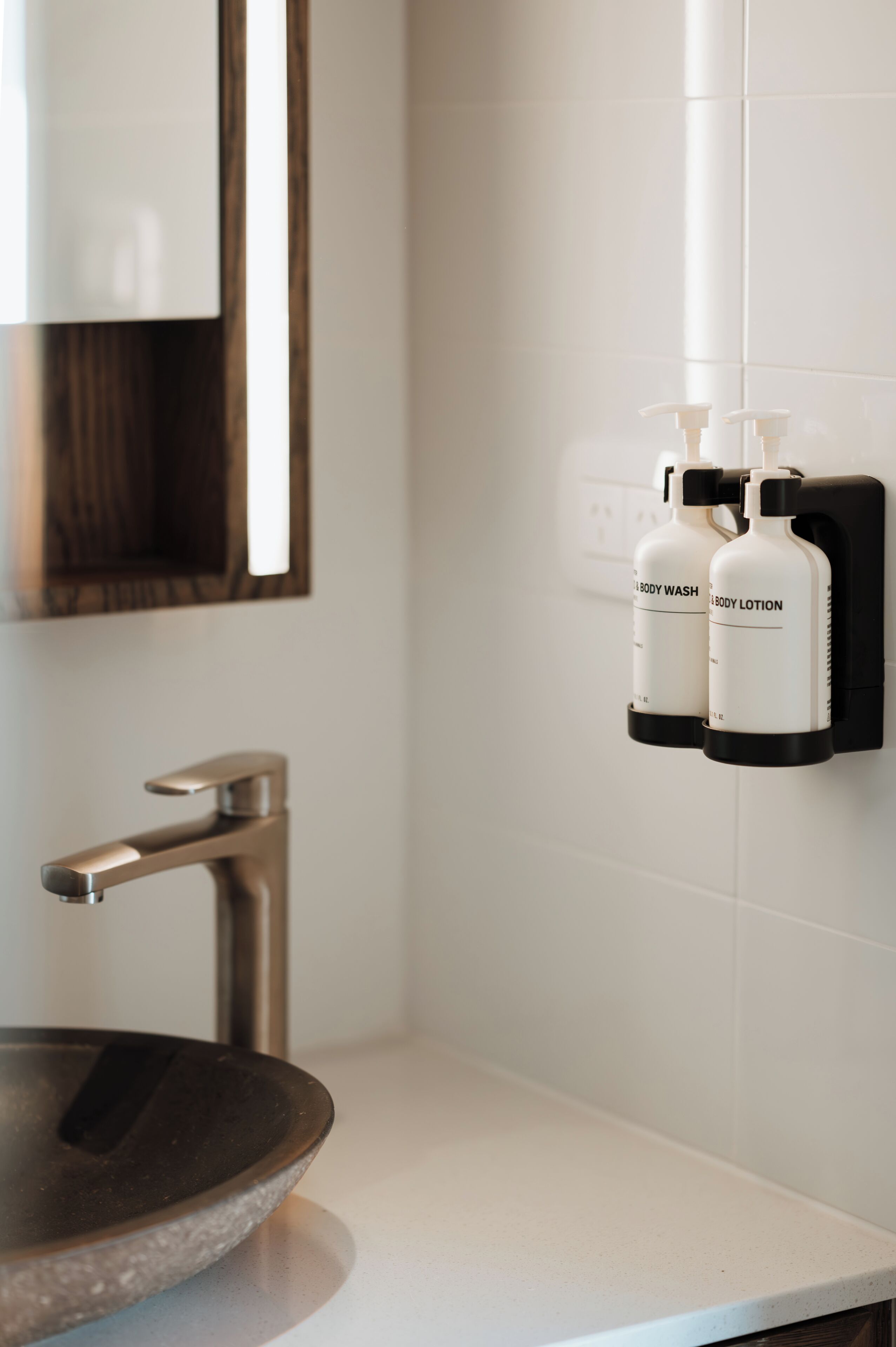 A modern bathroom with a vessel sink, a wall-mounted faucet, and two bottles of body wash and lotion.