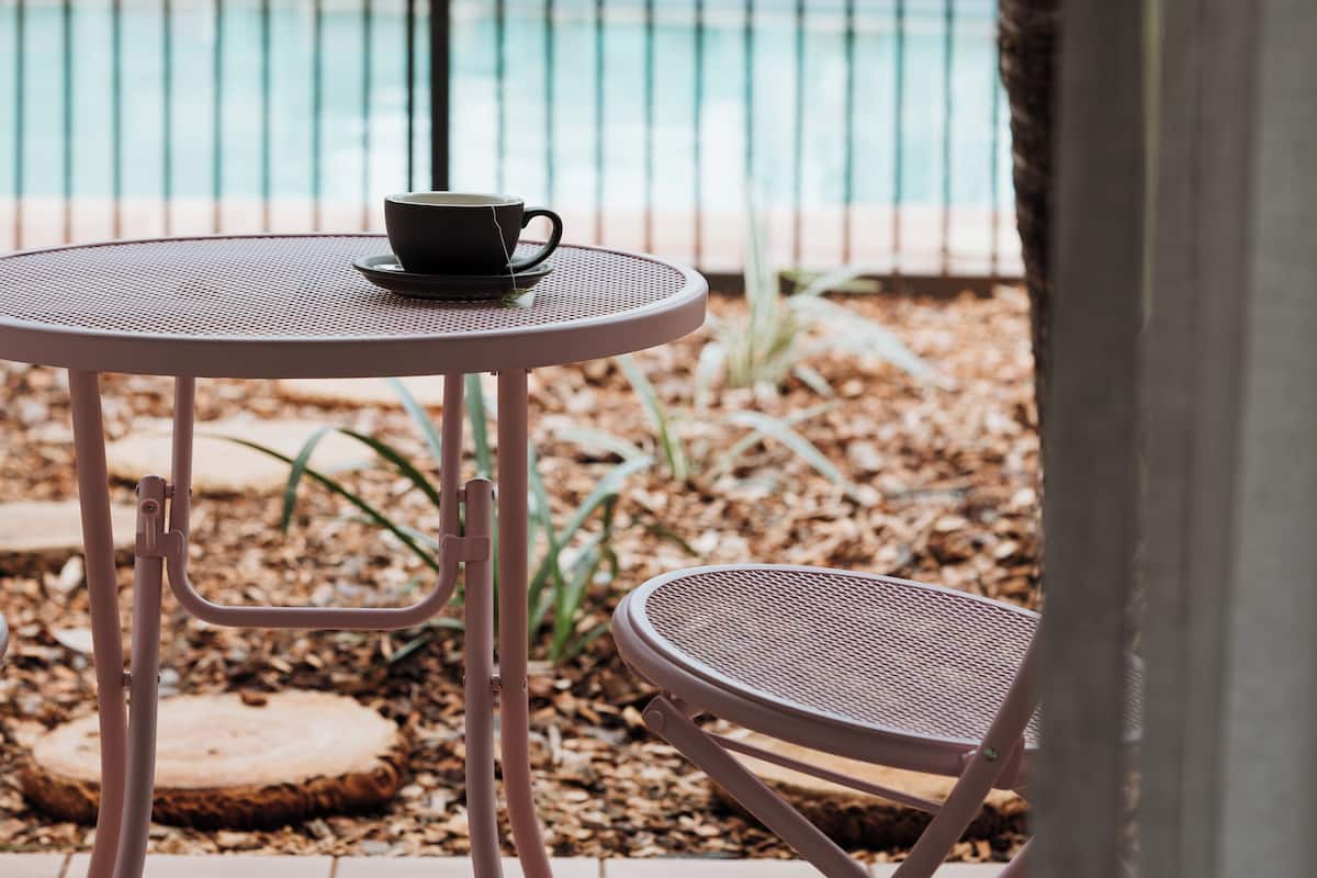Eine Terrasse mit Tisch und Stuhl, eine Tasse auf dem Tisch und ein Pool im Hintergrund.