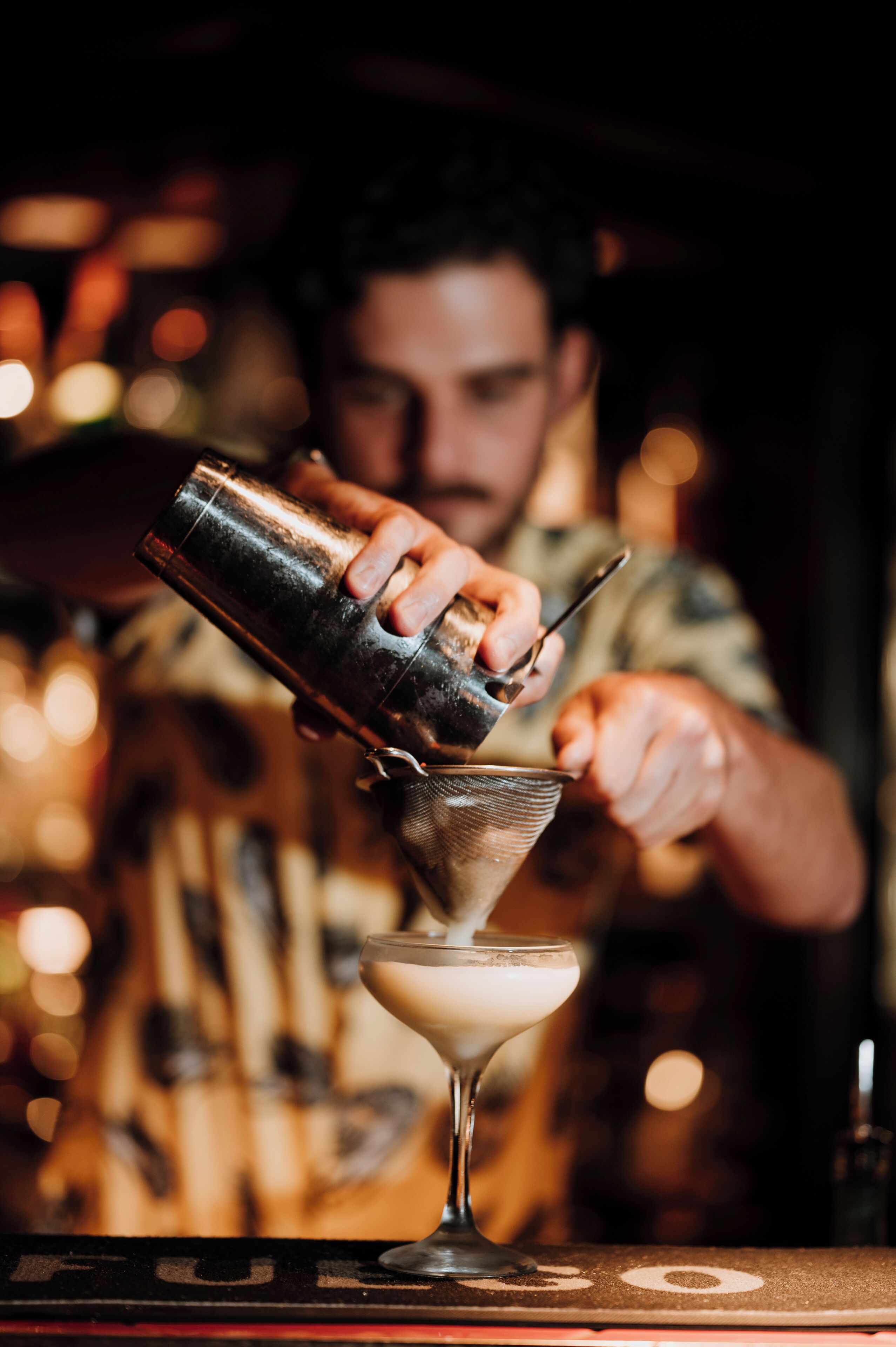 Un cantinero sirviendo una bebida en una copa de martini.