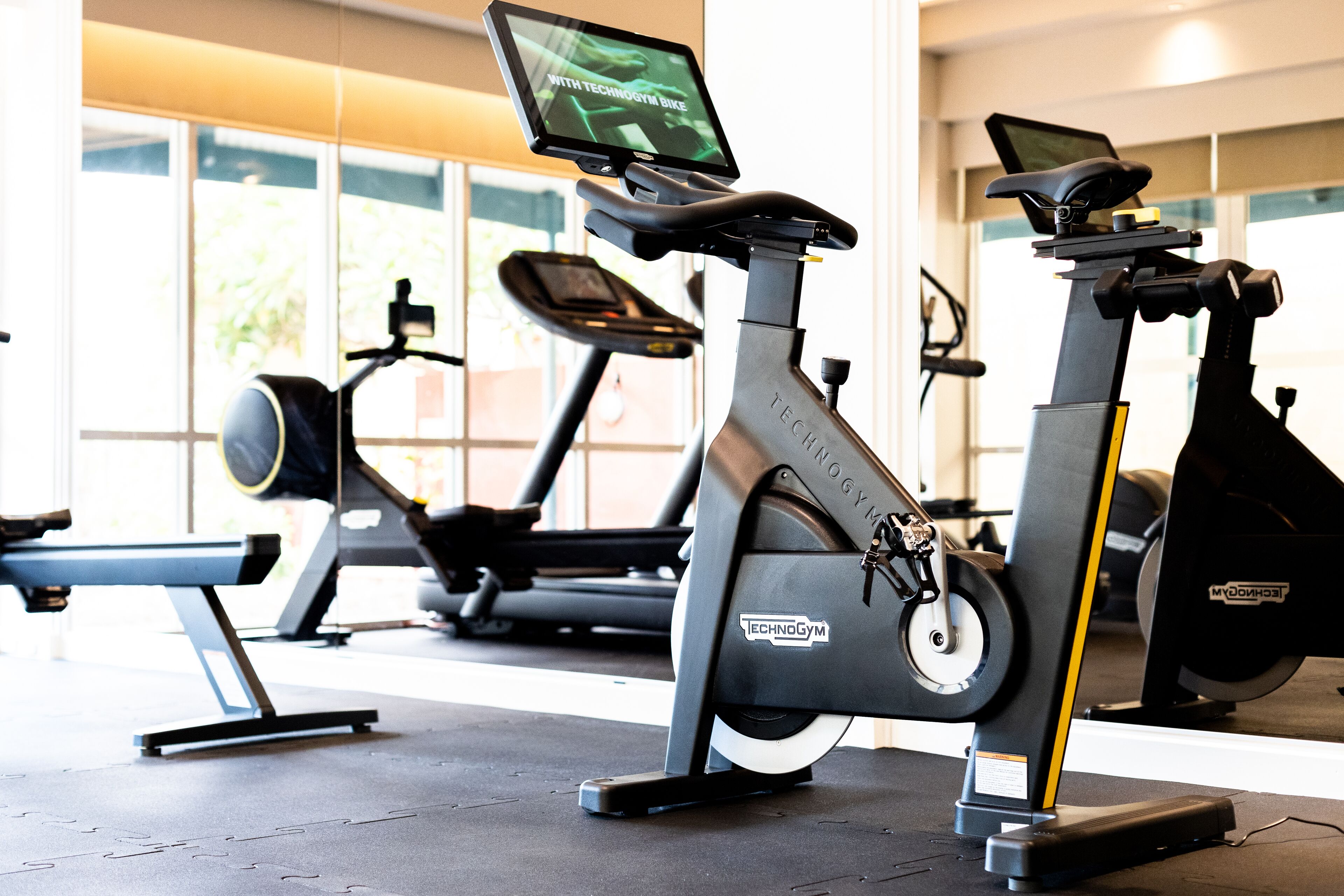 A stationary bike with a digital display and a treadmill in the background.