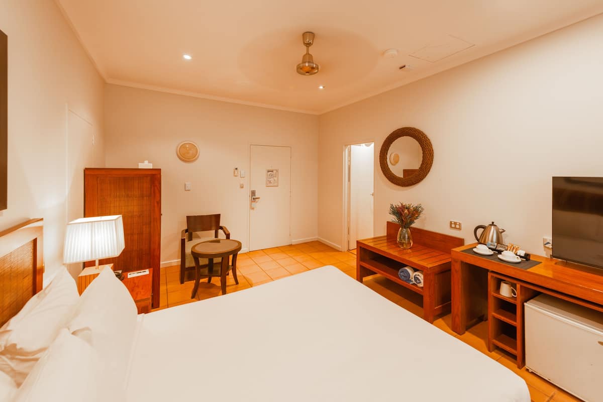 Ein Hotelzimmer mit einem Bett, einem Schreibtisch mit Fernseher, einem Sessel, einem kleinen Tisch mit einer Vase und einer Tür.