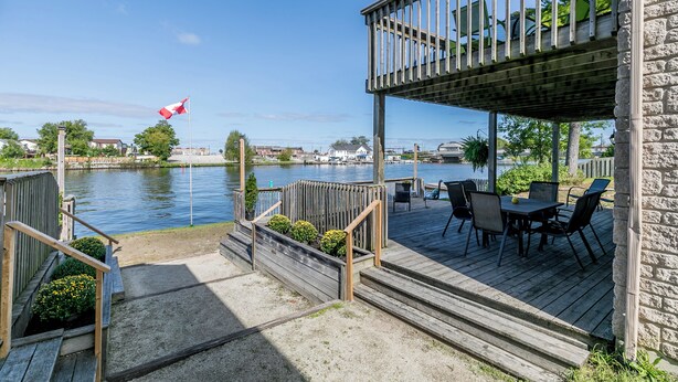 A wooden deck with a table and chairs, overlooking a body of water with a flag.