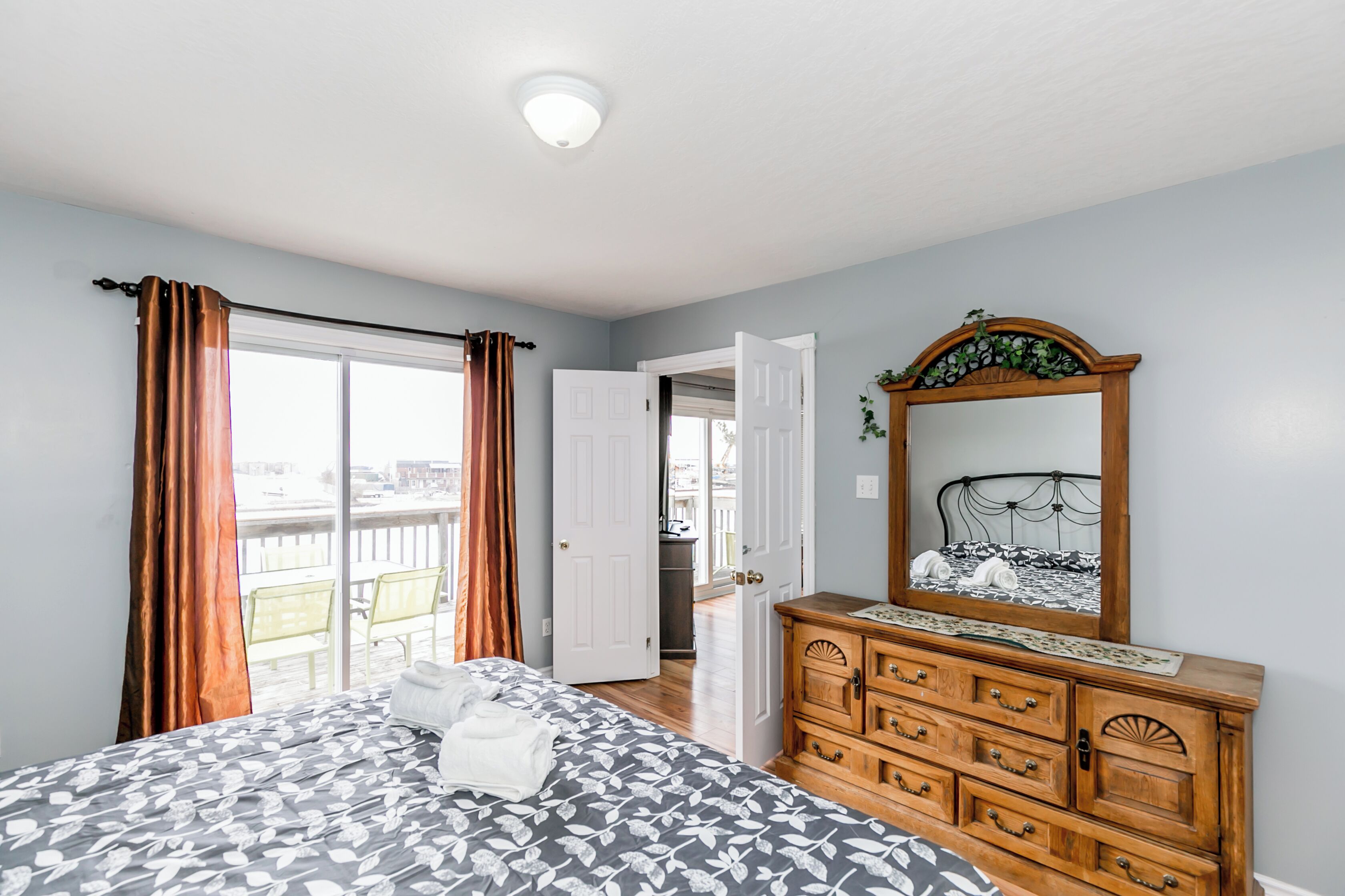 Een slaapkamer met een bed, een dressoir, een spiegel en een deur naar een balkon.