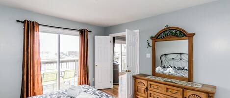 Een slaapkamer met een bed, een dressoir, een spiegel en een deur naar een balkon.