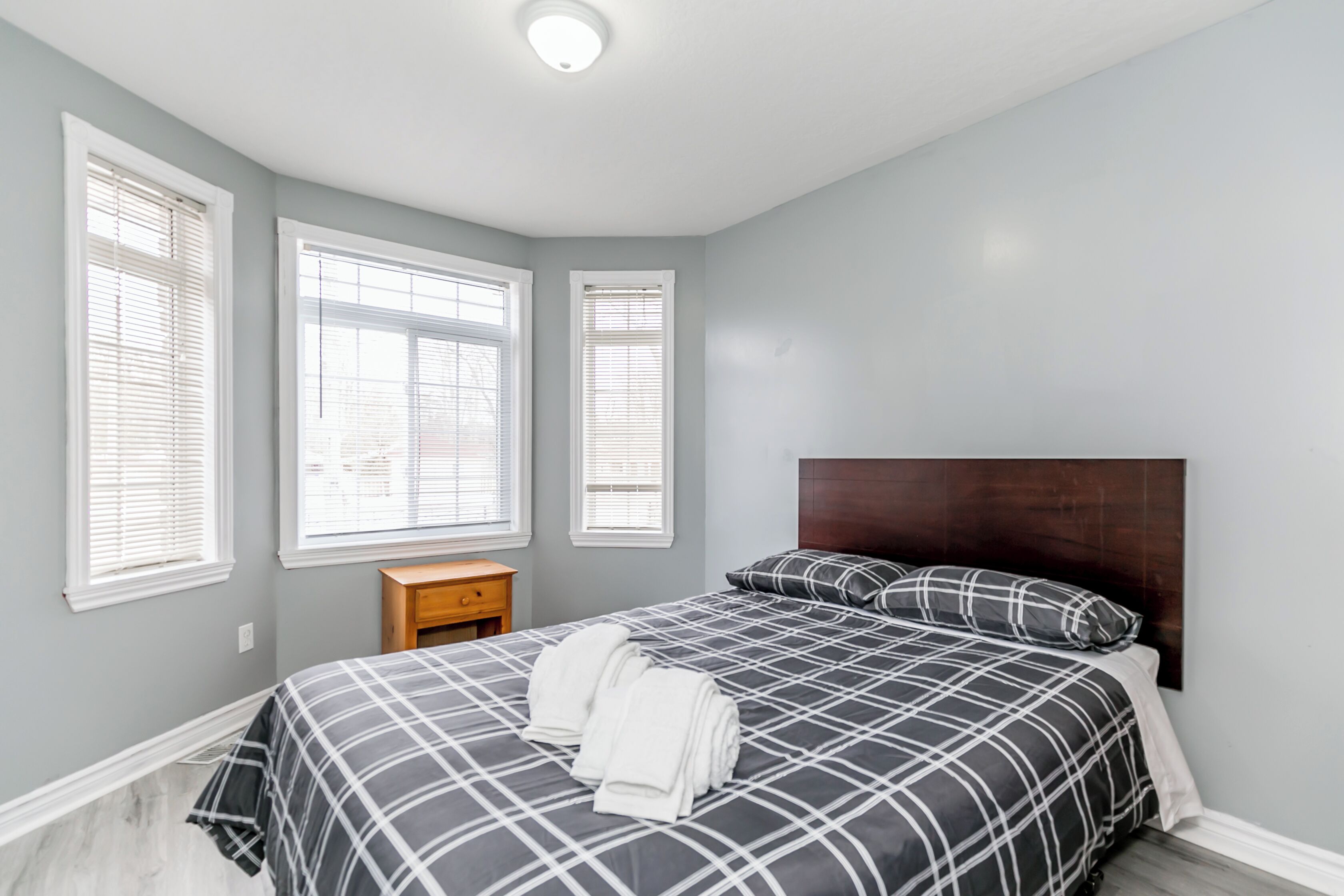 A bedroom with a bed, three windows, a nightstand, and a headboard.