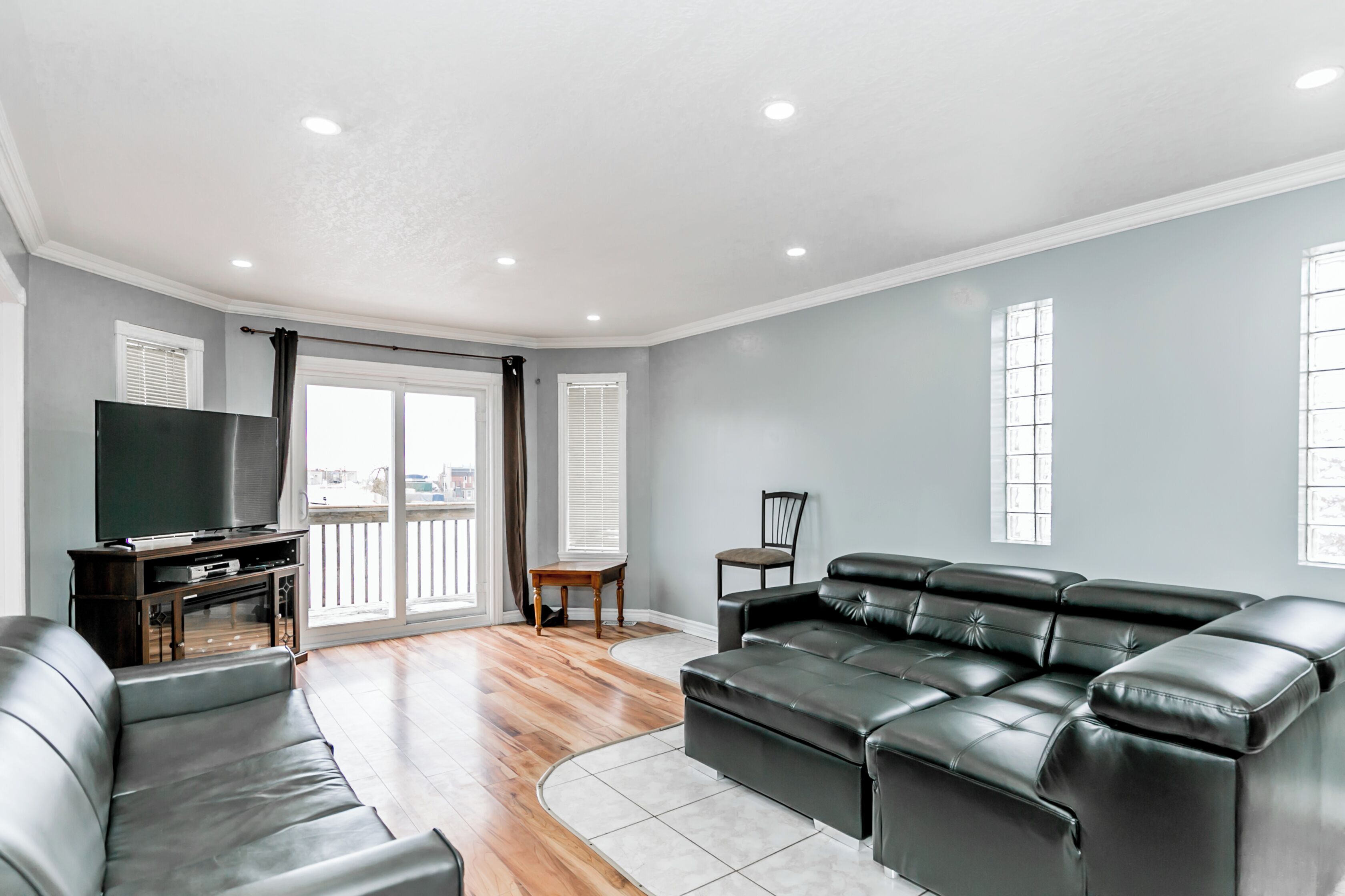 A spacious living room with a large black leather sofa, a flat-screen TV, and a wooden entertainment unit.