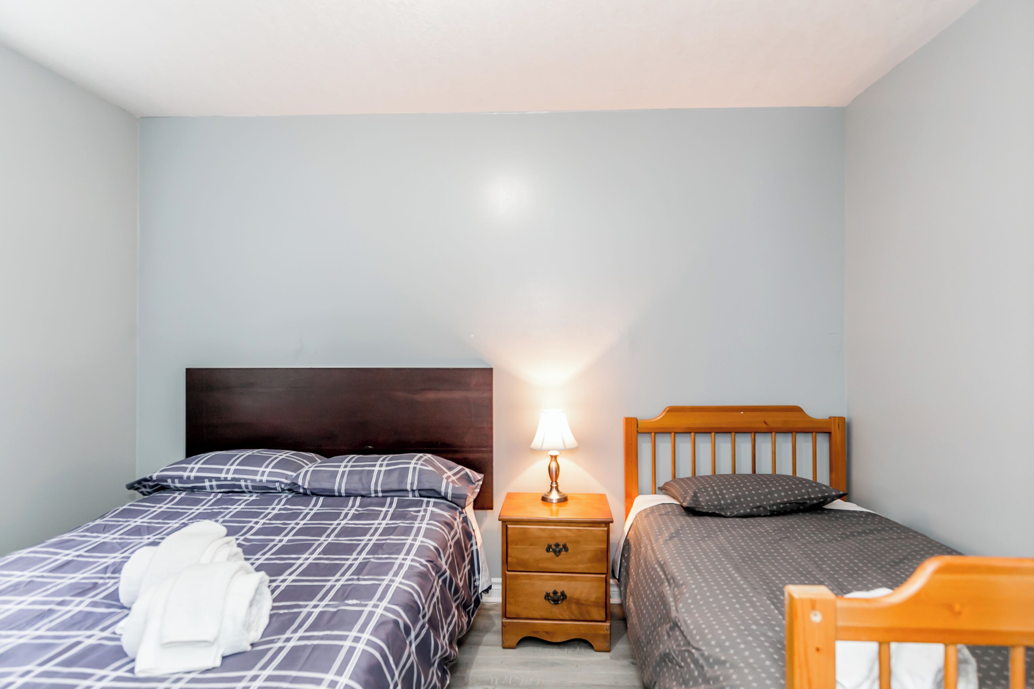 A bedroom with two beds, a nightstand with a lamp, and a rolled-up towel on the floor.