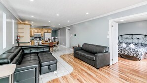 A modern living room with a sectional sofa, a single sofa, and a bed with a patterned bedspread.