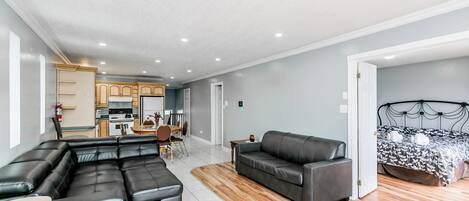 A modern living room with a sectional sofa, a single sofa, and a bed with a patterned bedspread.