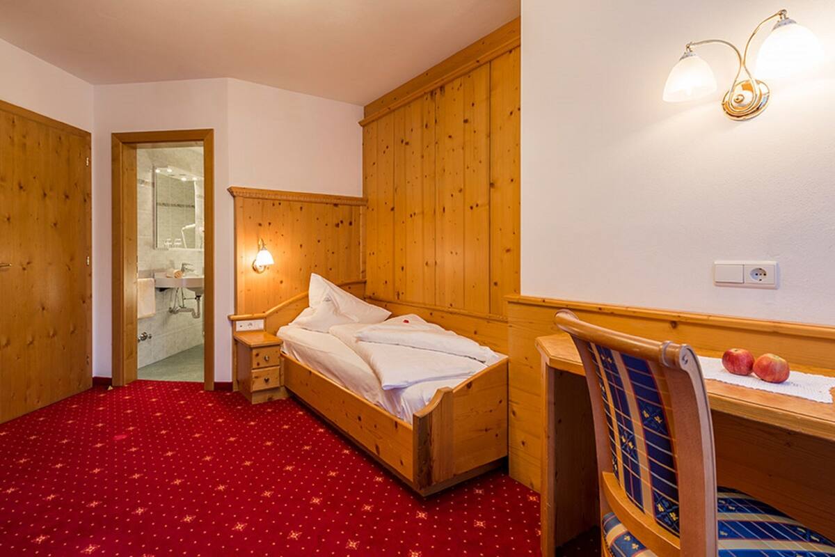 Habitación de madera con cama, escritorio y silla. Hay un espejo y una lámpara en la pared.