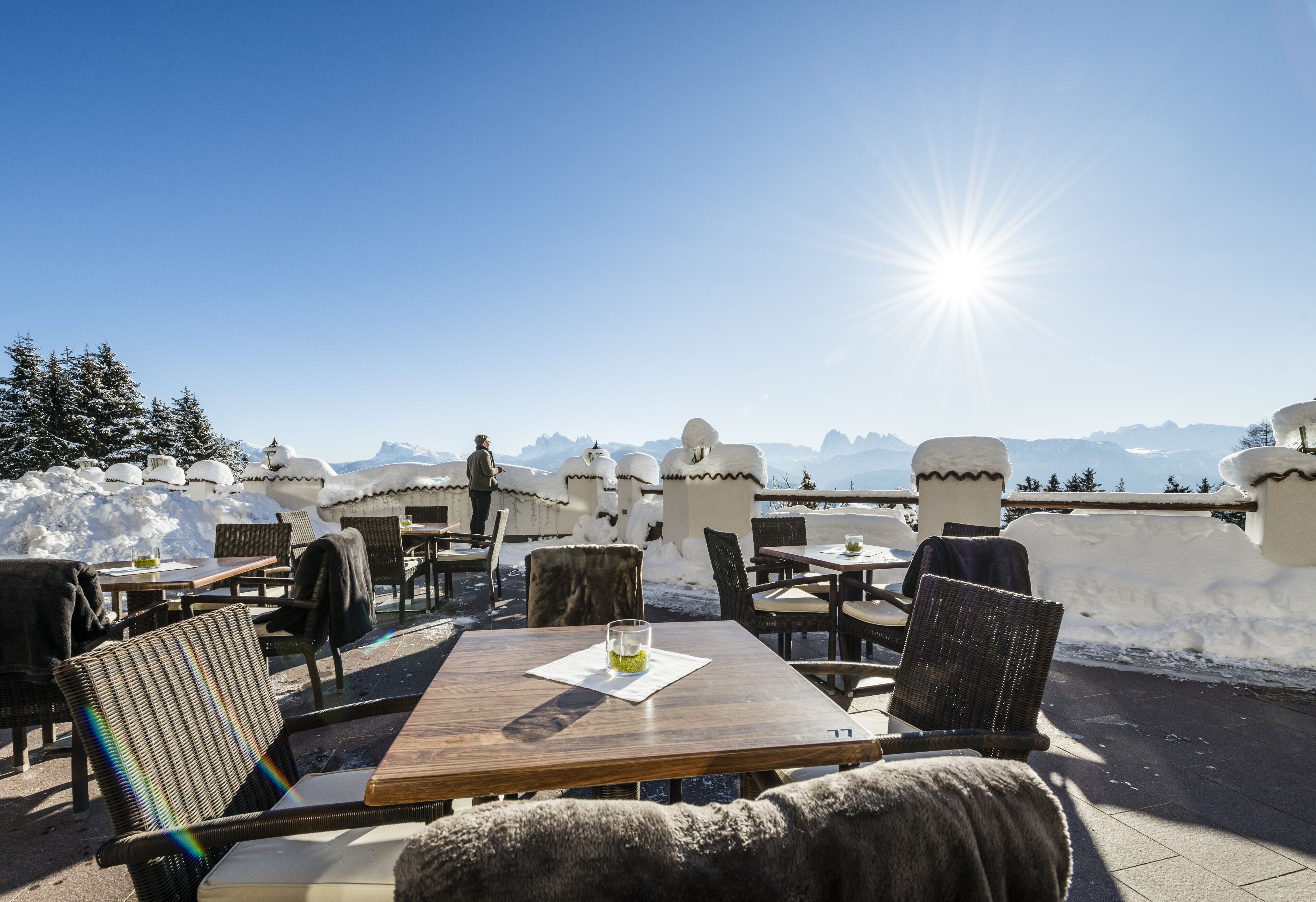 An outdoor seating area with tables and chairs, a glass of drink, and a snowy mountain backdrop.