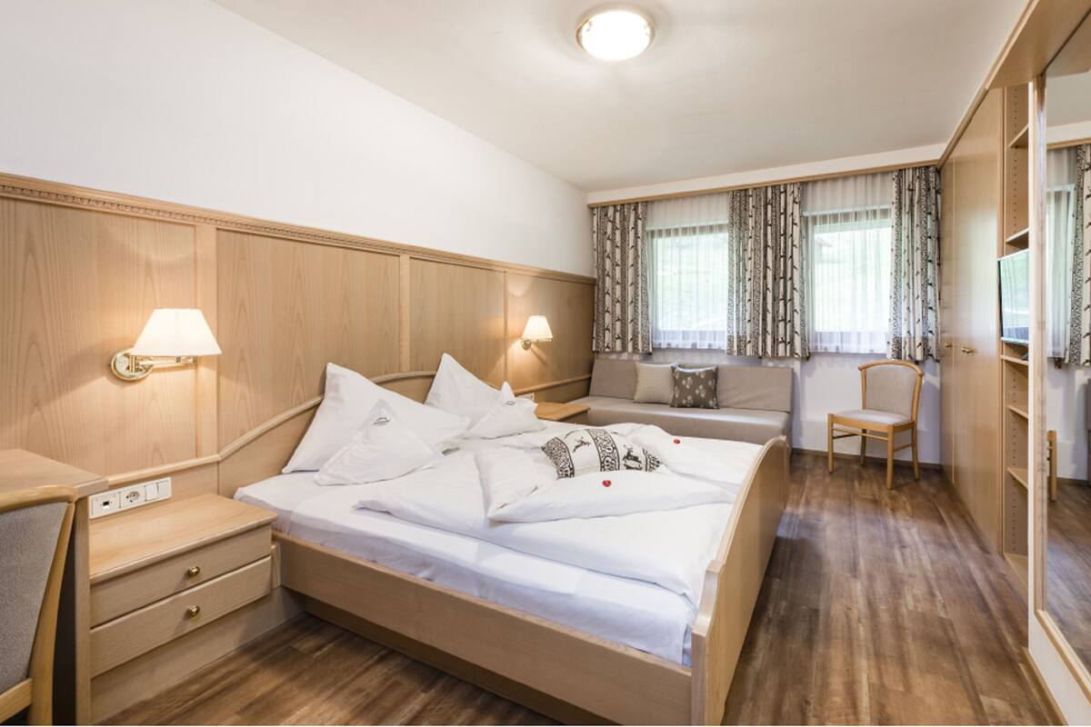 Una habitación de hotel con una cama grande, mesitas de noche, una silla, un sofá y una ventana con cortinas.