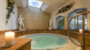 Un área de spa con un jacuzzi, paredes de piedra y estatuas decorativas.