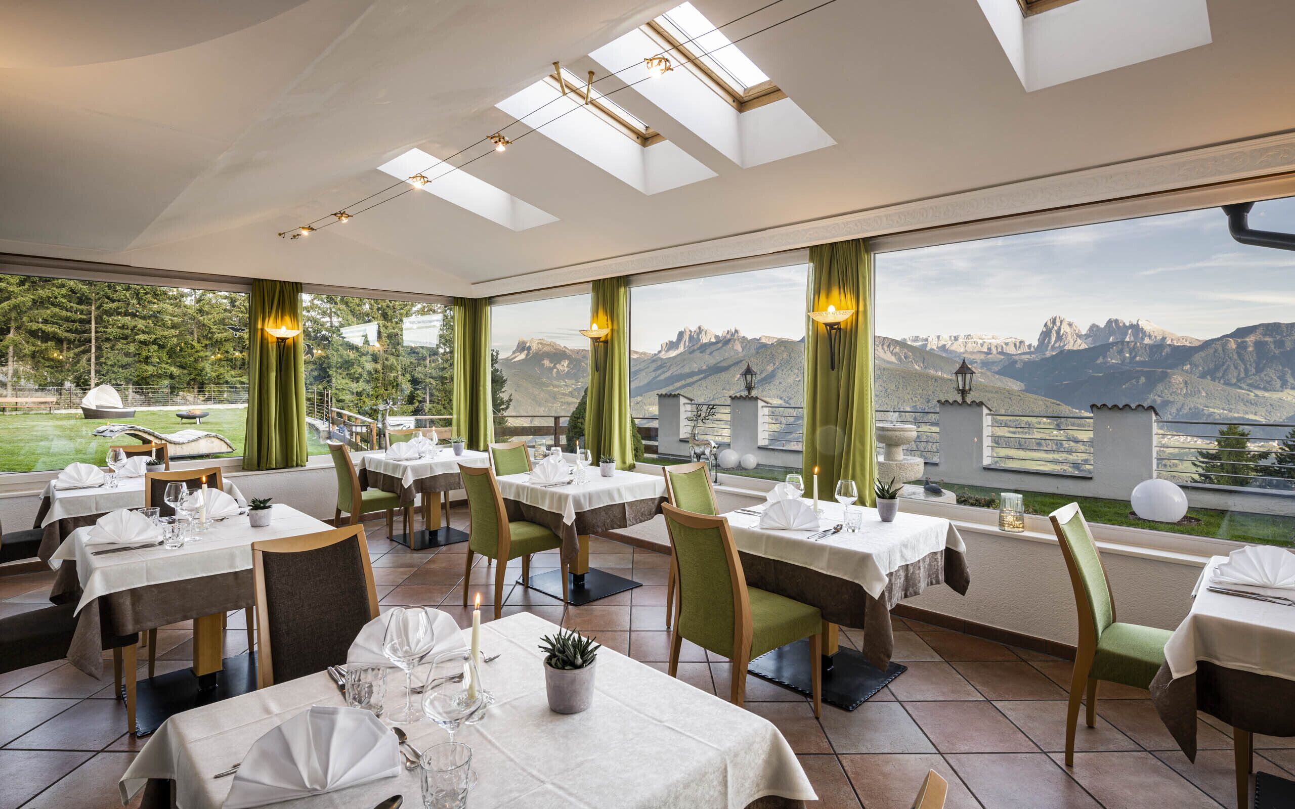A restaurant with multiple tables set for dining, large windows offering mountain views, and skylights on the ceiling.