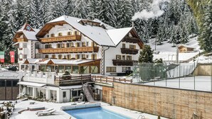 Un hotel con zona de piscina, mobiliario de exterior y un telesilla al fondo.