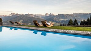 Piscina con sillones de descanso y vistas a montañas.