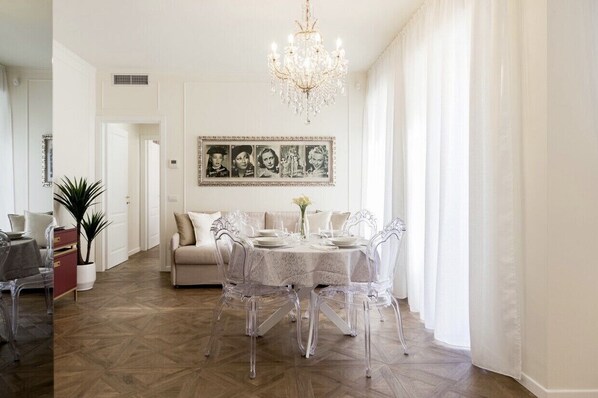 Un coin repas avec une table ronde, des chaises transparentes, un lustre et un mur décoré d’un ensemble de photos encadrées.