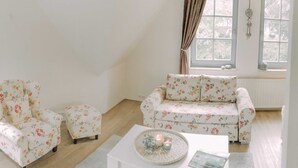 A living room with a floral sofa, matching armchair, and ottoman. A white coffee table with decorative items is in the center.