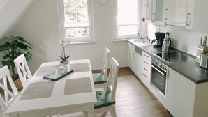 A compact kitchen with white cabinetry, a dining table with chairs, and a large window providing natural light.
