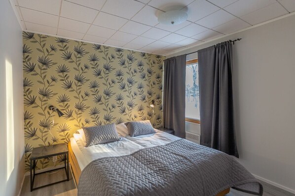 A bedroom with a bed, a nightstand, a lamp, and a window with curtains.