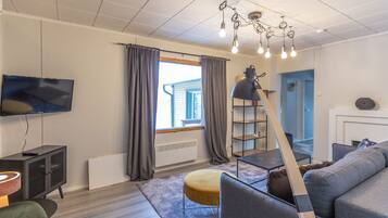 Un salon moderne doté d’un téléviseur à écran plat, d’un canapé gris, d’une table basse en bois et d’une lampe originale.