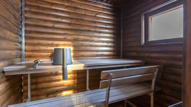 Interior de una cabaña de madera con un banco, una mesa y una ventana.