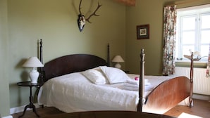 Un dormitorio con cama con dosel, una cabeza de ciervo montada en la pared y una ventana con cortinas florales.