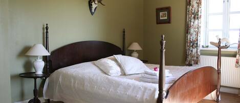A bedroom with a four-poster bed, a mounted deer head on the wall, and a window with floral curtains.