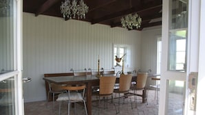 Comedor con mesa de madera, sillas de mimbre, una lámpara de araña y una ventana decorada con un gallo.