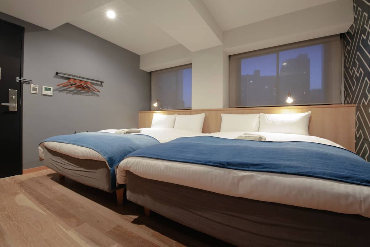 Habitación de hotel con dos camas, cabecera de madera, ventana grande y una lámpara en el techo.