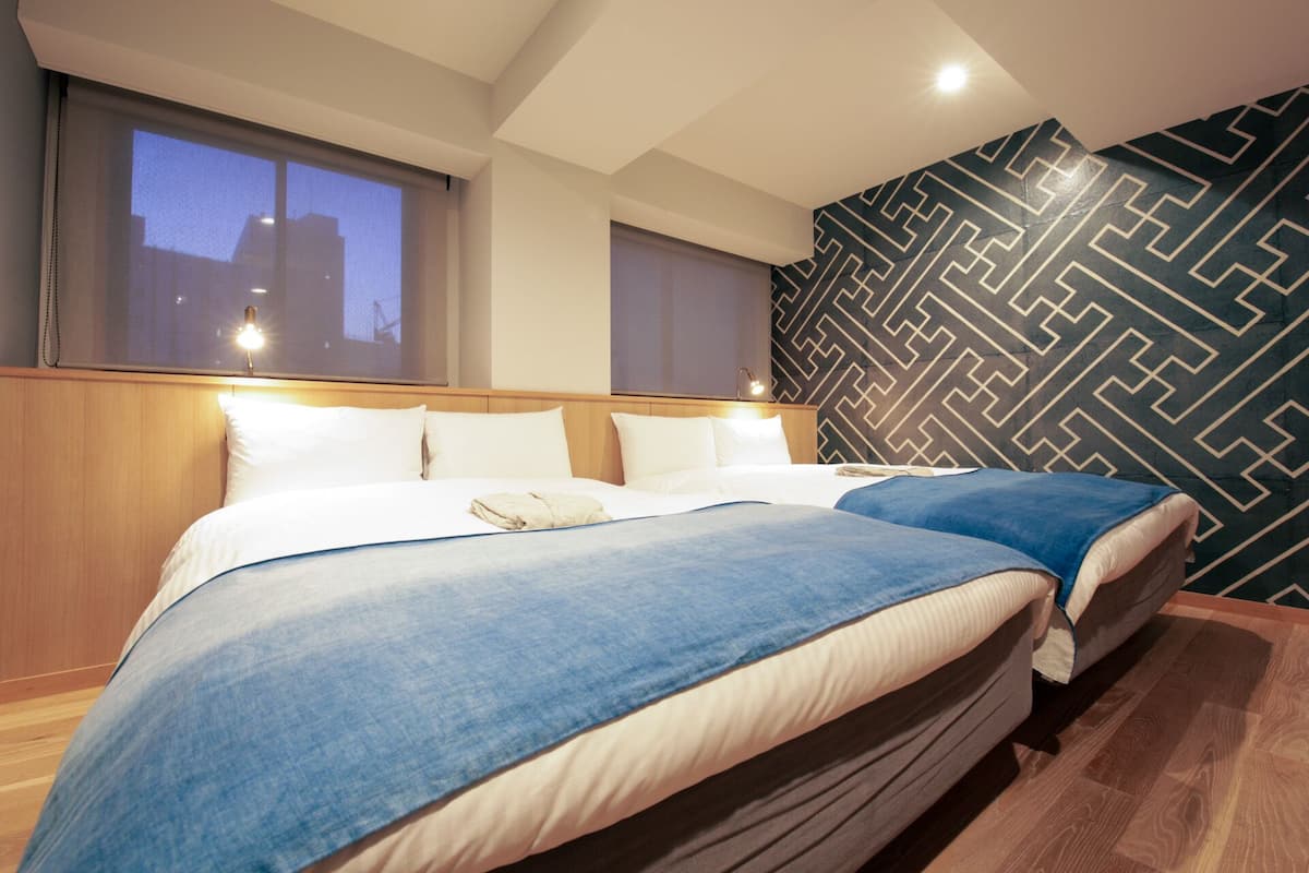 Habitación de hotel con dos camas, un ventanal grande y un papel tapiz de diseño geométrico.