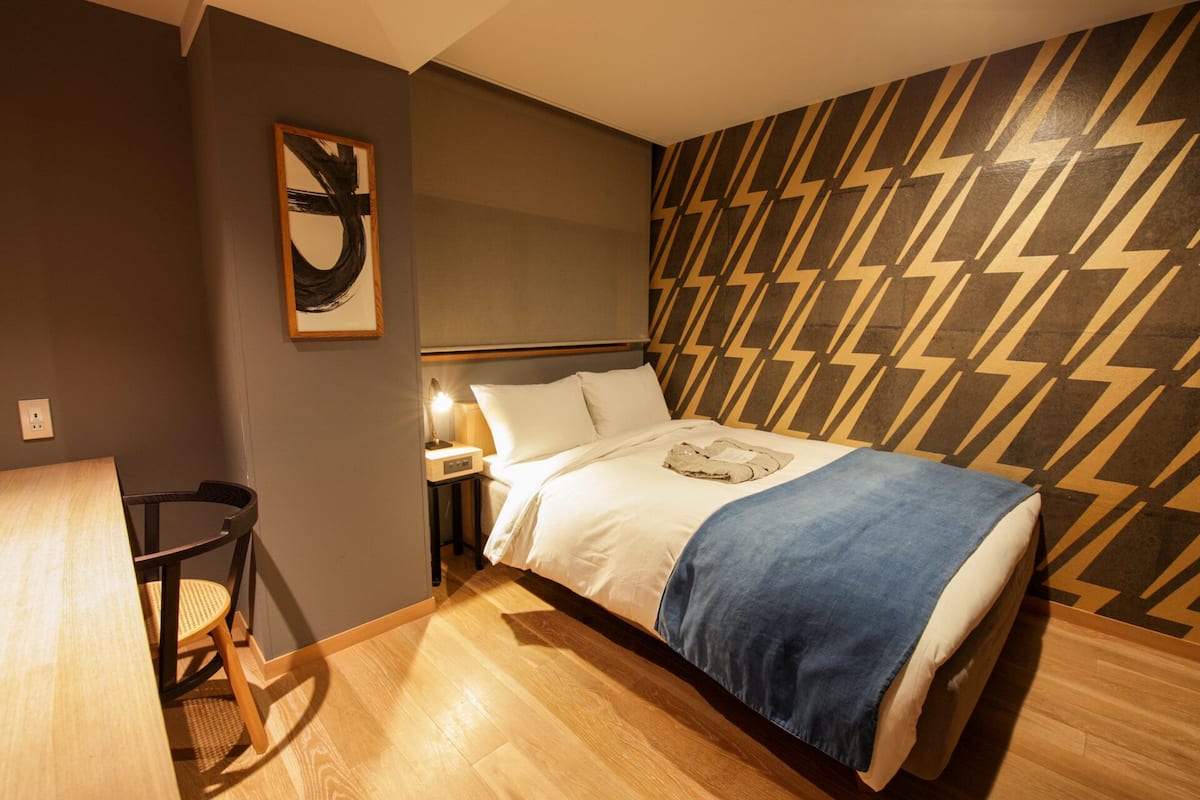 Una habitación de hotel moderna con cama, mesita de noche, lámpara y un papel tapiz estampado.