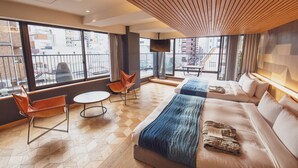 Et moderne hotelværelse med en stor seng, en sofa, en stol og et lille bord. Store vinduer med udsigt over byen.