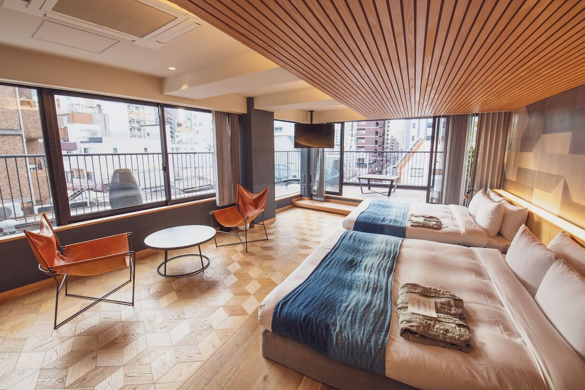 Una habitación de hotel moderna con una cama grande, un sofá, una silla y una mesita. Amplias ventanas con vistas a la ciudad.