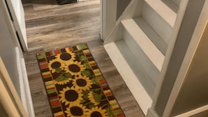 A hallway with wooden flooring, a colorful sunflower-patterned rug, and a white staircase.
