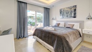 A modern bedroom with a large bed, a ceiling fan, and a balcony with curtains. - Beautiful 4 Bed Villa ⭐ Heated Pool ⭐ 650m Beach & Dunas de Artola (Marbella)