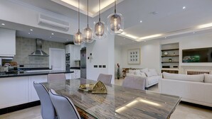 A modern kitchen with a central island, pendant lighting, and a dining area with a glass-top table. - Beautiful 4 Bed Villa ⭐ Heated Pool ⭐ 650m Beach & Dunas de Artola (Marbella)