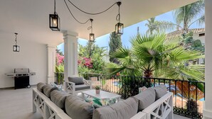 An outdoor patio with a white cushioned sofa, a small table, and hanging lanterns. - Beautiful 4 Bed Villa ⭐ Heated Pool ⭐ 650m Beach & Dunas de Artola (Marbella)