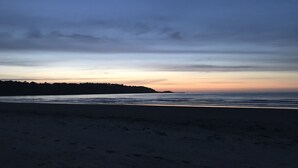 A beach with a calm sea and a distant landmass under a twilight sky.