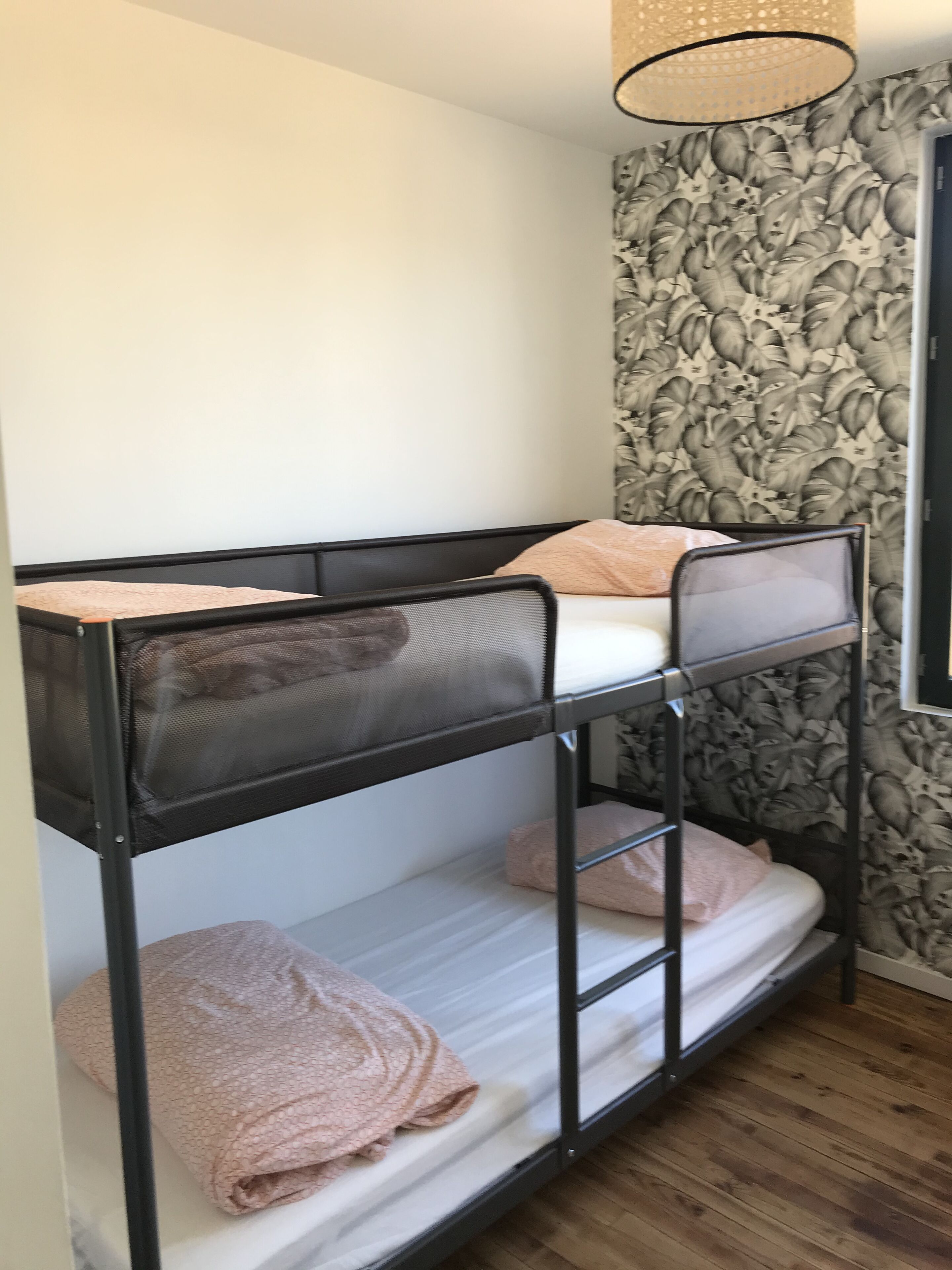 Un lit superposé avec une tête de lit en treillis, une fenêtre à cadre noir et un papier peint à motifs floraux.
